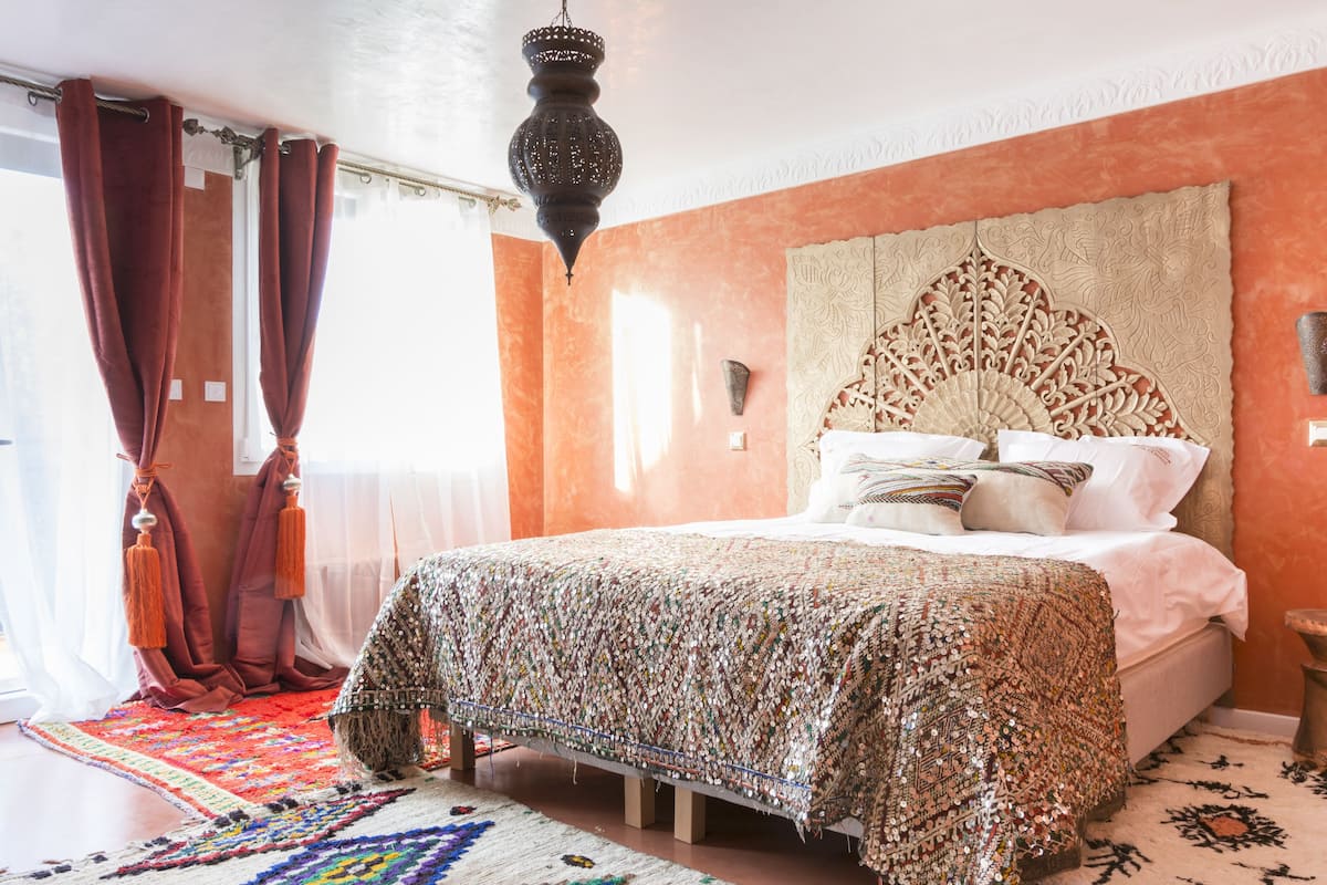 Een slaapkamer met een groot bed, een decoratief hoofdeinde en een hanglamp.