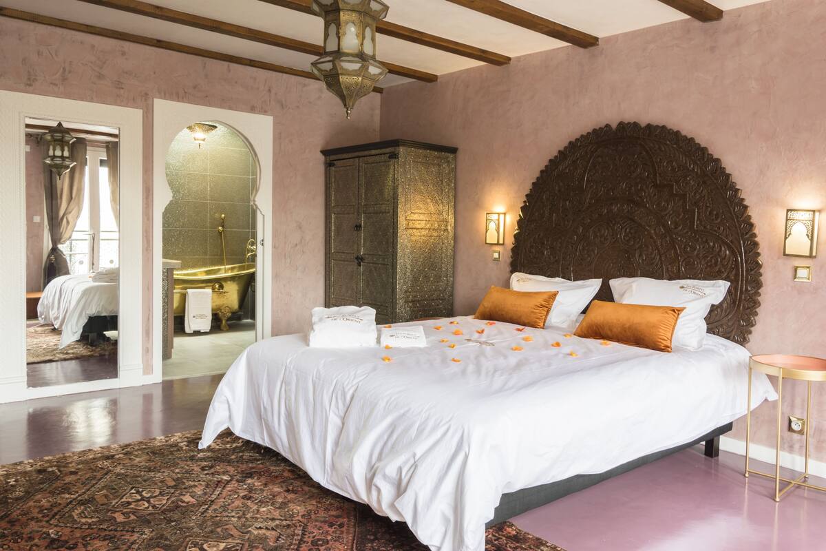 Een ruime slaapkamer met een groot bed, een houten hoofdbord en een decoratieve spiegel.