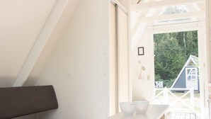A modern interior with a bench, a table with two bowls, and a view of a house through a door.