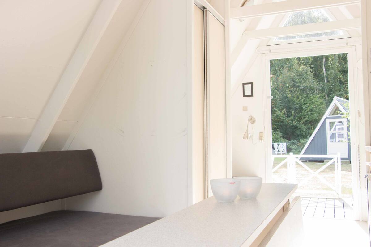 Ein modernes Interieur mit einer Bank, einem Tisch mit zwei Schalen und Blick auf ein Haus durch eine Tür.
