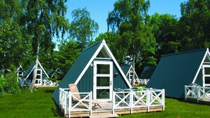 A row of triangular cabins with white railings and a deck, surrounded by lush green trees.