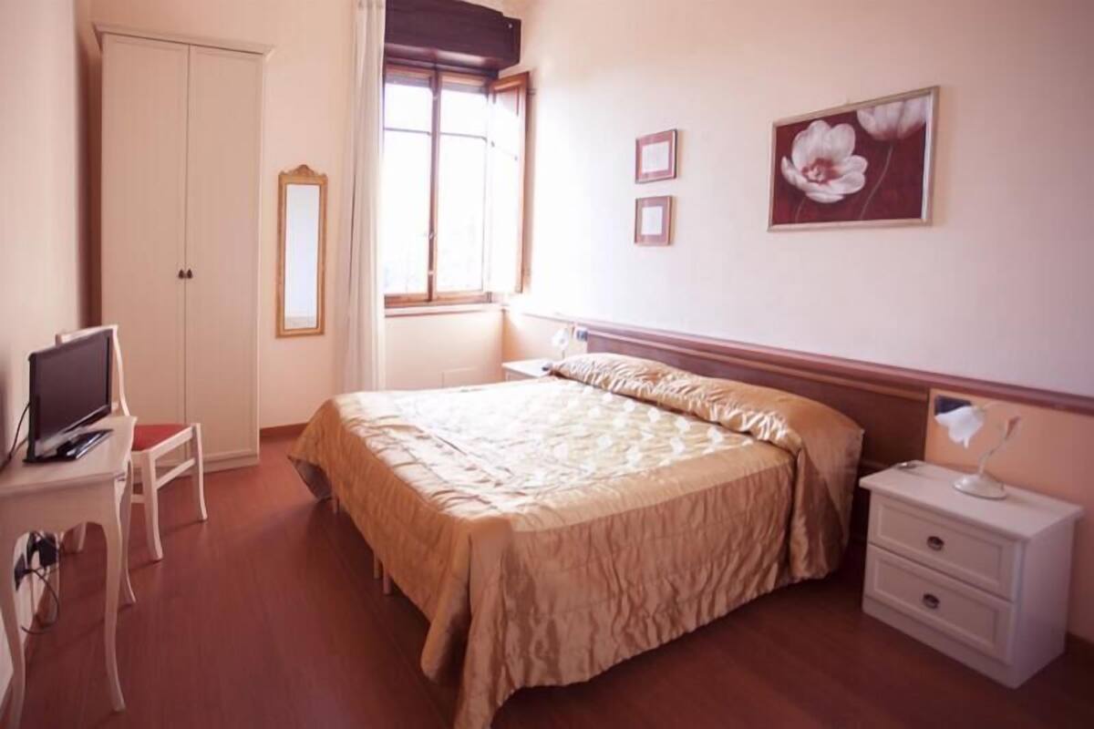 A bedroom with a bed, a desk, a chair, a nightstand, and a window.