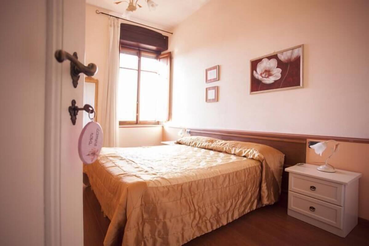 A bedroom with a bed, a nightstand, a window, and a wall-mounted picture.