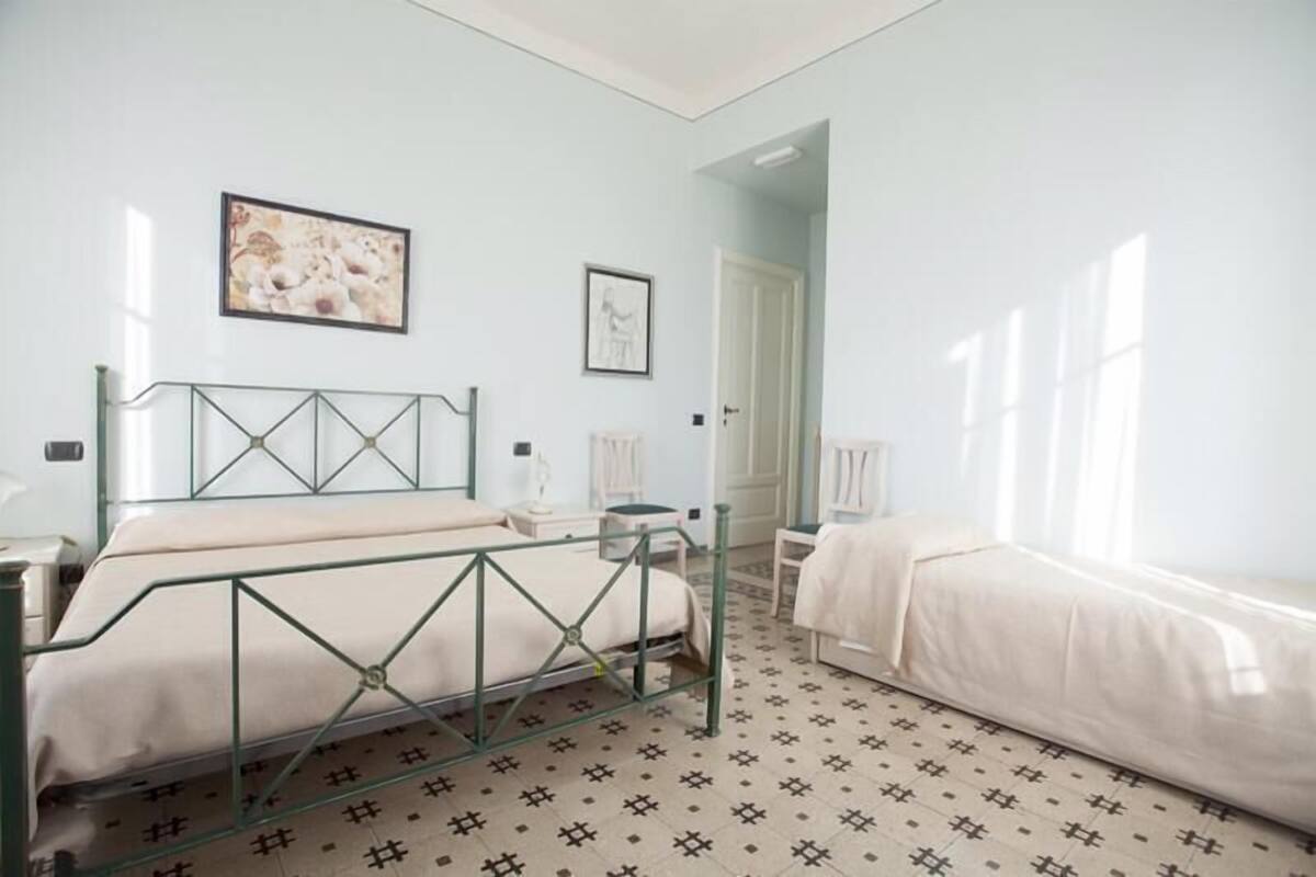 A bedroom with a bed, a chair, a bedside table, a mirror, and a door leading to another room.