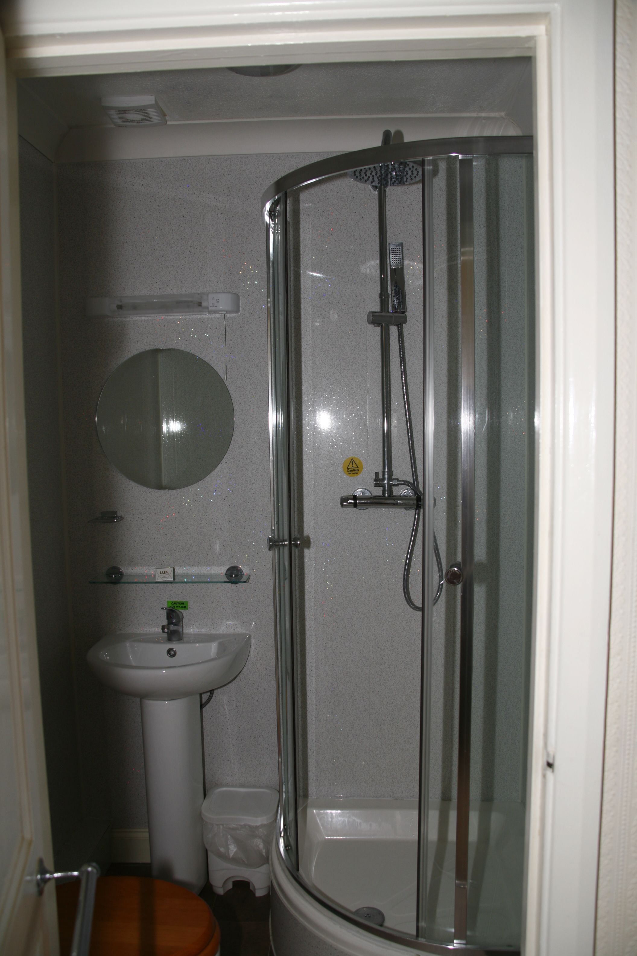A bathroom with a glass-enclosed shower, a pedestal sink, a toilet, and a mirror.
