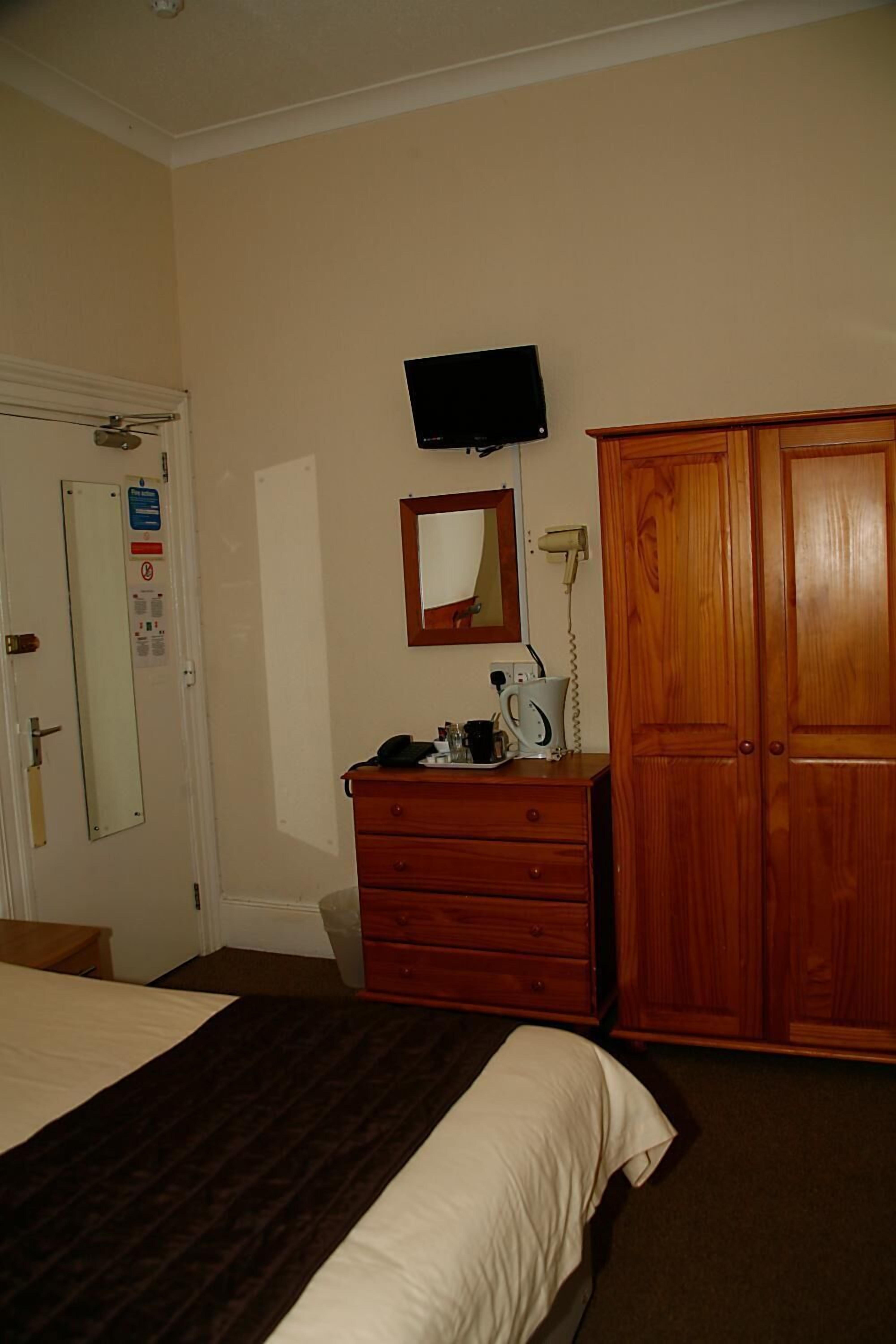 A hotel room with a bed, dresser, mirror, television, and wardrobe.