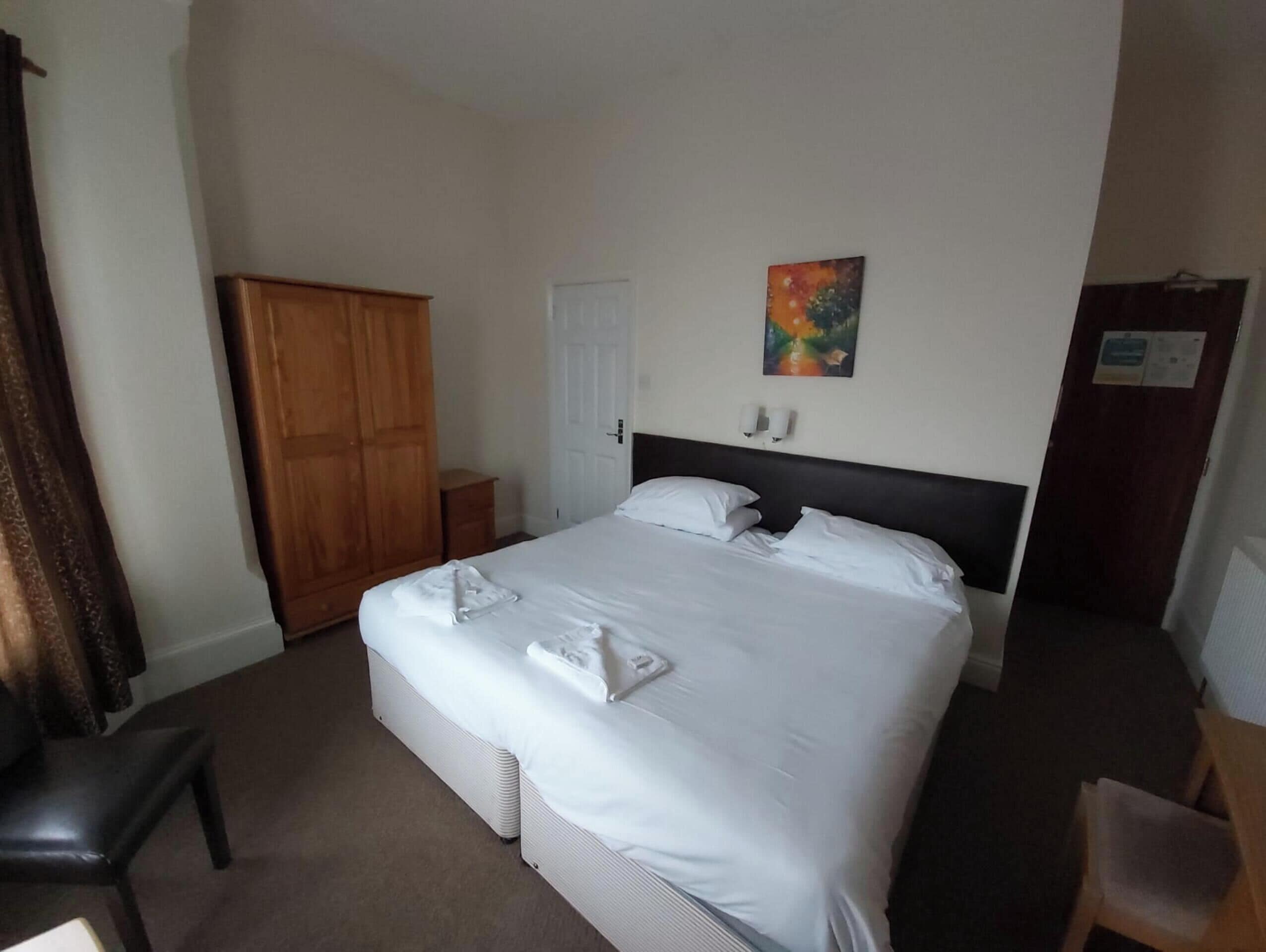 A hotel room with a bed, a wardrobe, a desk, and a painting on the wall.