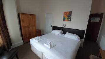 A hotel room with a bed, a wardrobe, a desk, and a painting on the wall.