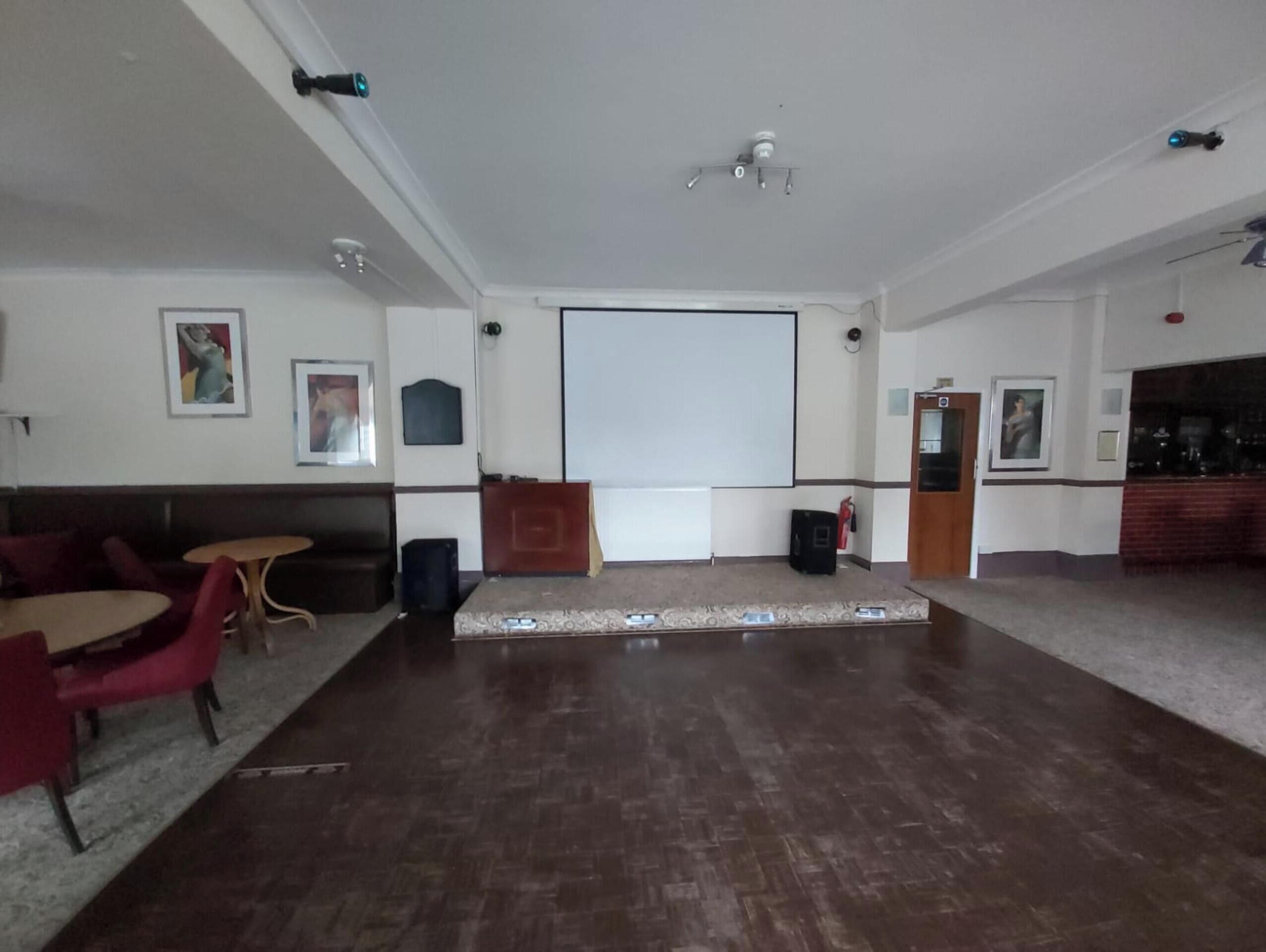 A spacious room with a large white projection screen, a wooden podium, and a red couch.