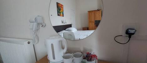 Habitación de hotel con un espejo redondo, un hervidor blanco, dos tazas y una bandeja con bolígrafos y blocs de notas.