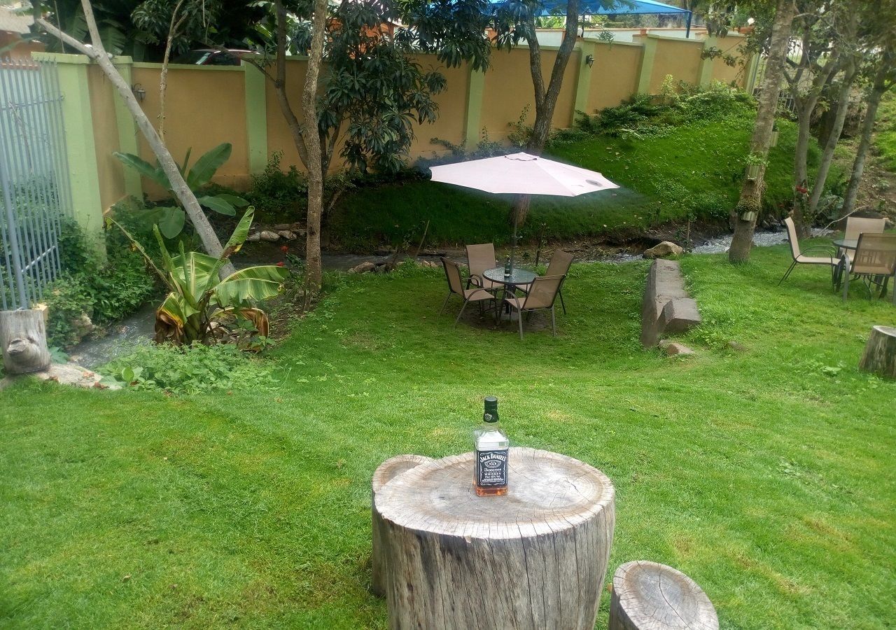A backyard with a wooden table, a bottle of Jack Daniel's whiskey, and a patio umbrella.