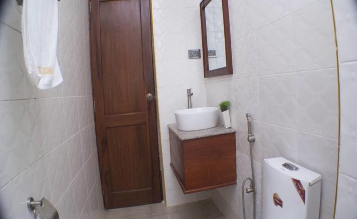 A bathroom with a wooden door, a white sink, a mirror, and a towel hanging on the wall.