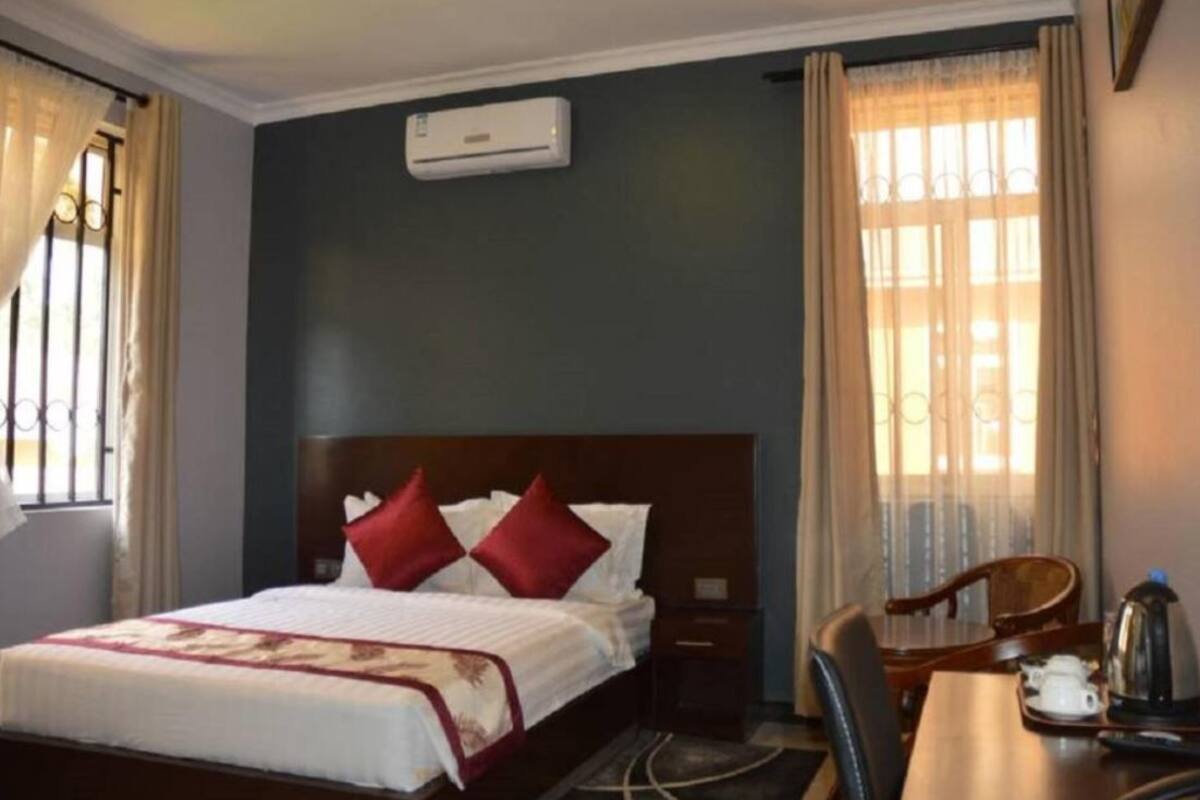 Una habitación de hotel con cama, escritorio con hervidor y aire acondicionado en la pared.