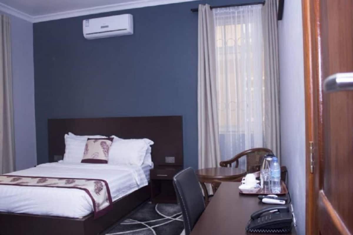 Habitación de hotel con cama, escritorio, silla, teléfono y una botella de agua.