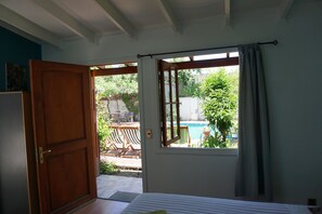 A bedroom with a wooden door, a window with curtains, a bed, and a view of an outdoor area with a pool and furniture. - Ventana Sur Hostel (Santiago)