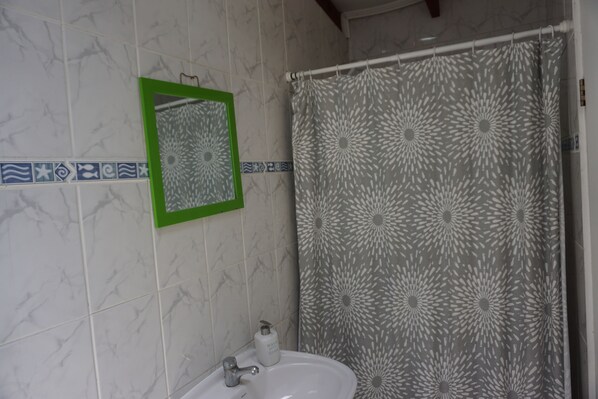 A bathroom with a white sink, a green-framed mirror, and a grey shower curtain with a floral pattern. - Ventana Sur Hostel (Santiago)