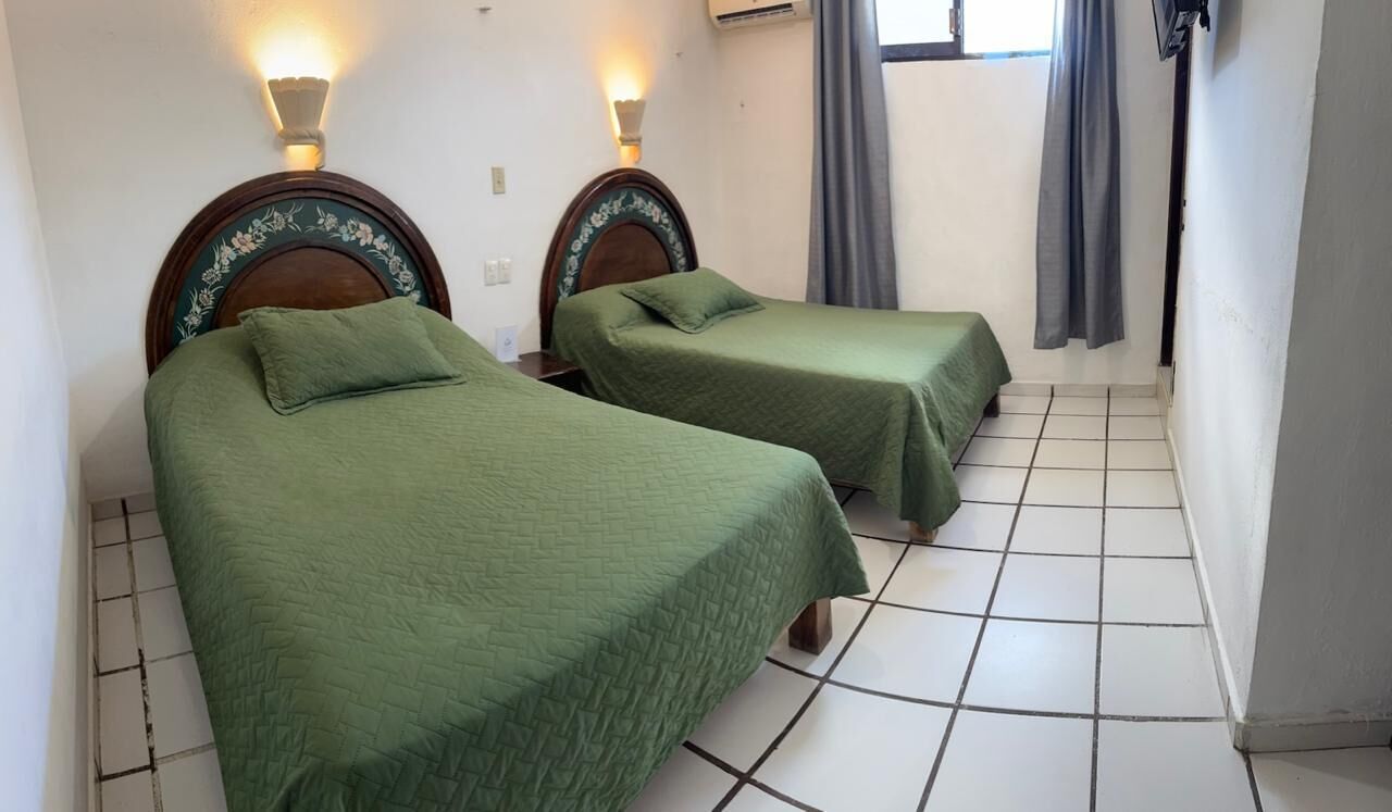 Two single beds with green bedding, wooden headboards, and wall-mounted lamps.