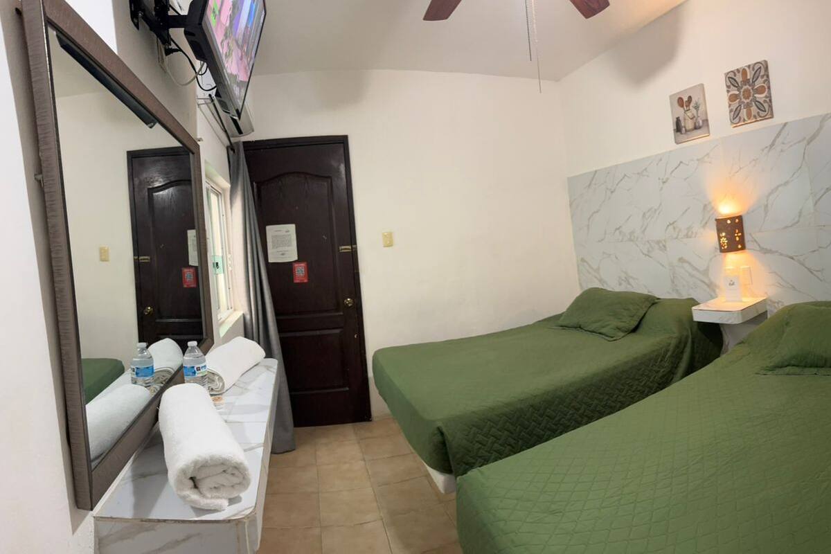A hotel room with two single beds, a bathroom with a mirror, a towel, and a wall-mounted light fixture.