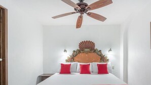 A hotel room with a bed, a ceiling fan, a decorative headboard, and wall-mounted lights.