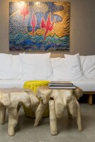 Una sala de estar moderna con un sofá blanco, taburetes de madera, una cesta amarilla tejida y un cuadro abstracto colorido en la pared.