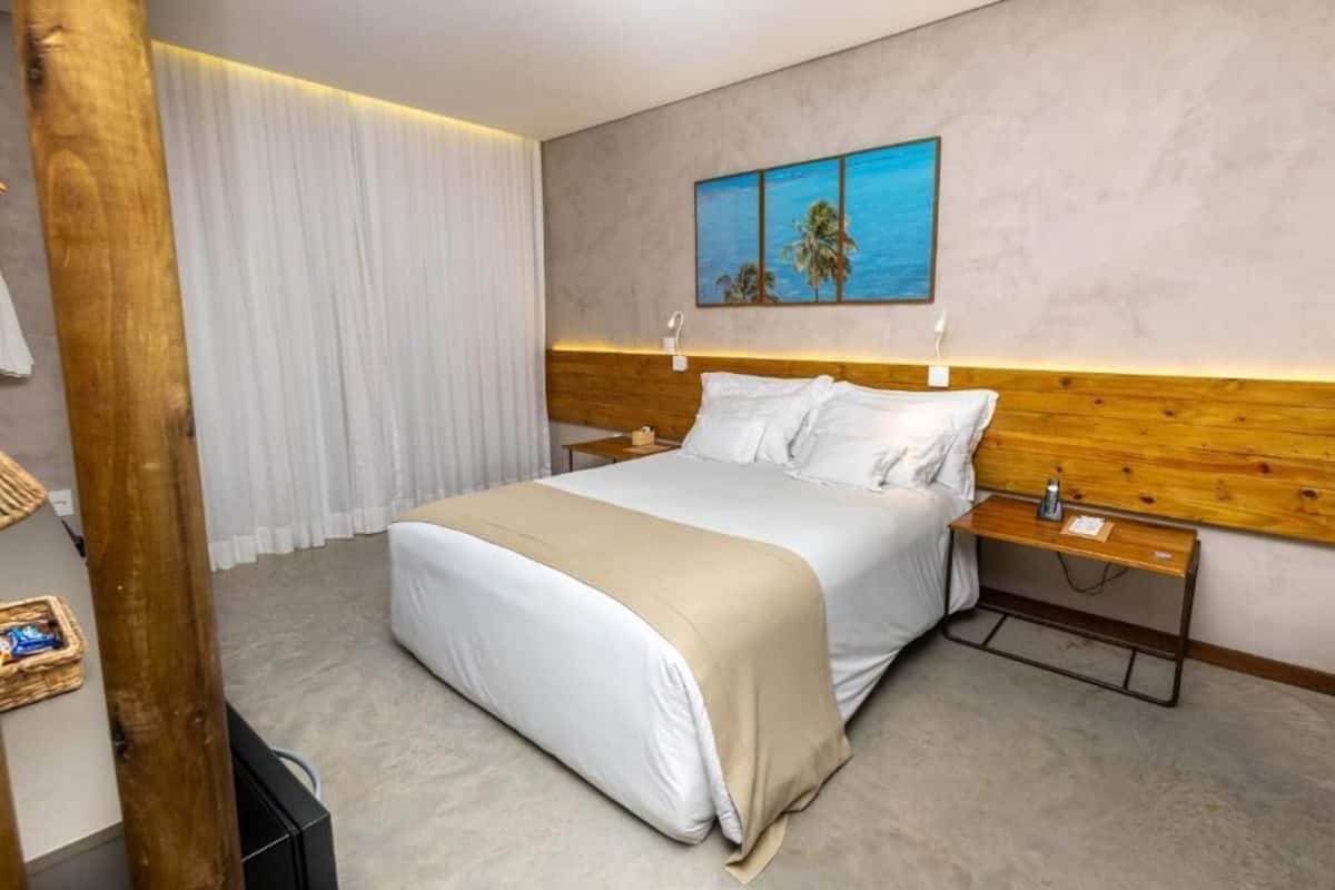 A hotel room with a large bed, a wooden headboard, a nightstand, and a painting of palm trees on the wall.