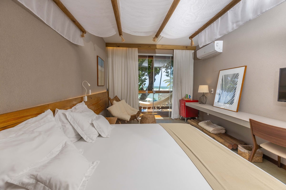 A hotel room with a large bed, a wooden headboard, a desk, a chair, a hammock, and a view of the outdoors.