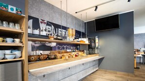 A modern kitchen area with a coffee station, shelves with kitchenware, and a wall-mounted TV.