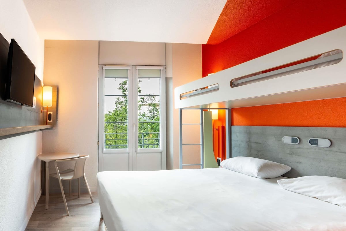 A modern hotel room with a bunk bed, a desk, and a TV.