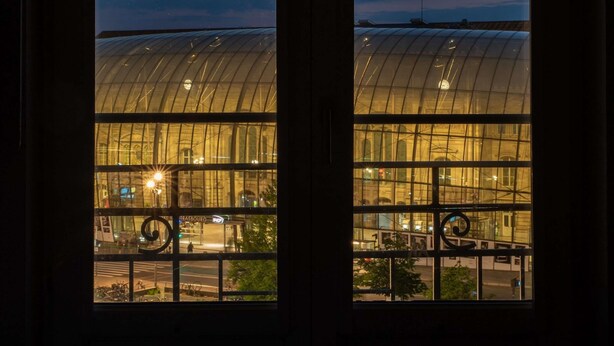 A view through a window of a modern building with a curved glass facade and a clock visible on the upper part.
