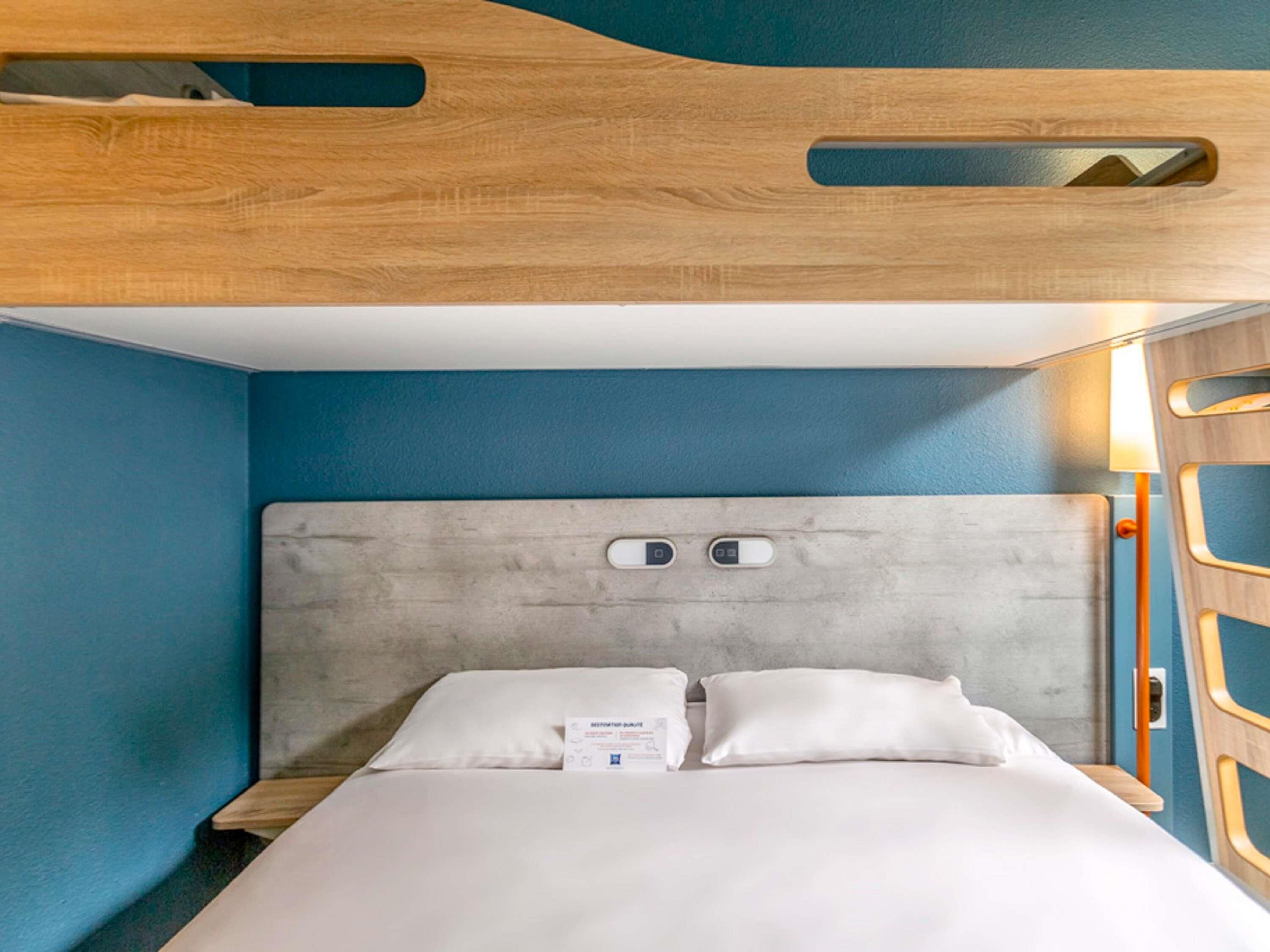 Une chambre d’hôtel moderne avec une tête de lit en bois, un lit recouvert de draps blancs et un mur d’accent bleu.