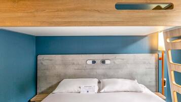 Une chambre d’hôtel moderne avec une tête de lit en bois, un lit recouvert de draps blancs et un mur d’accent bleu.