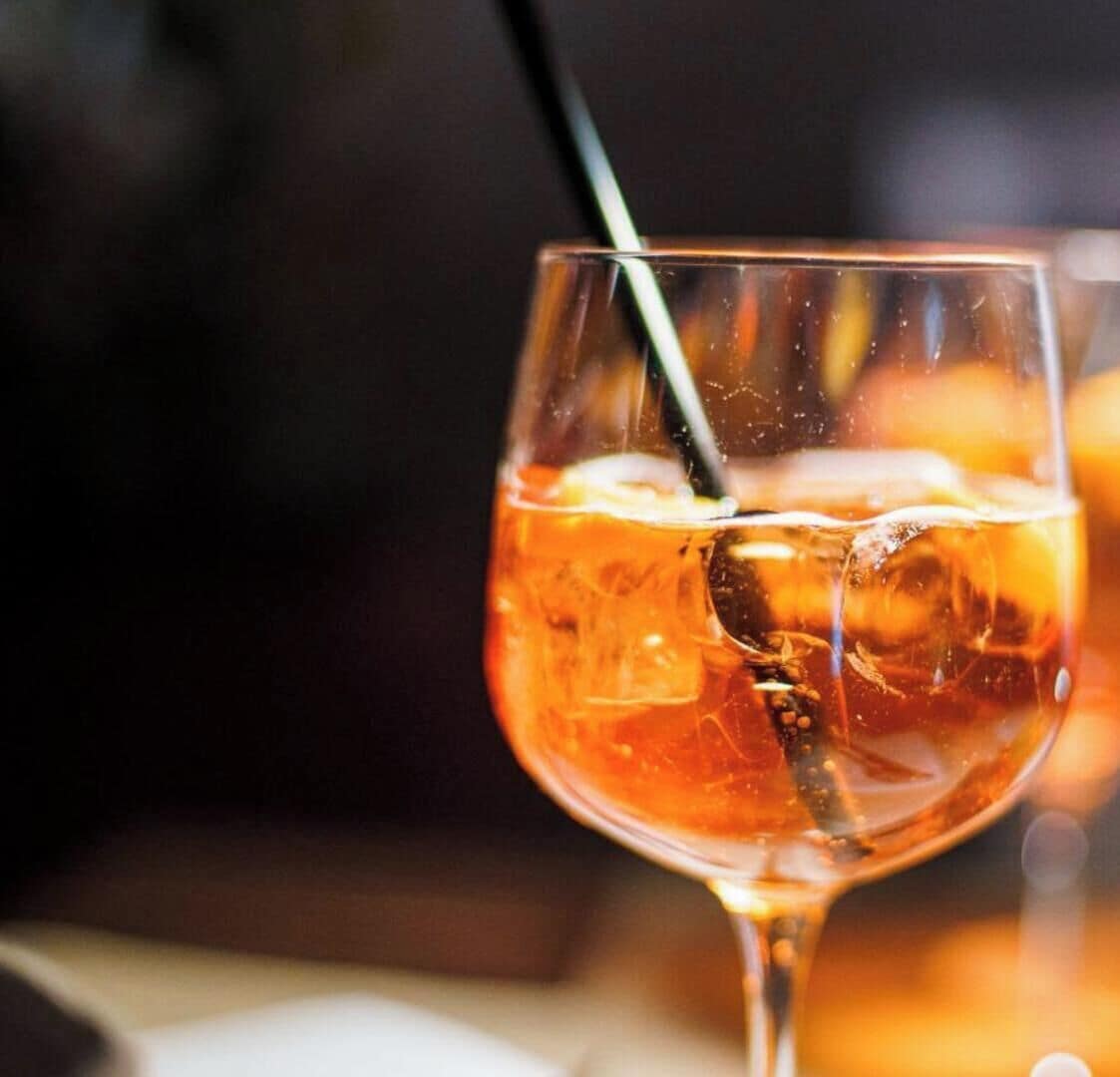 Un verre contenant une boisson ambrée, avec des glaçons et une paille, posé sur une surface.