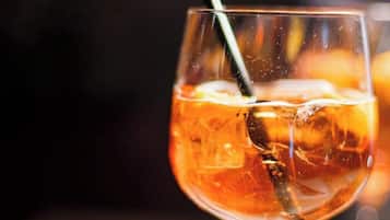 Un vaso de bebida color ámbar con cubitos de hielo y una pajita, sobre una superficie.