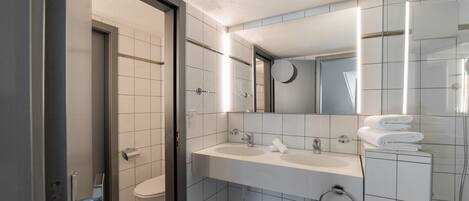 A modern bathroom with a toilet, two sinks, a mirror, and a towel rack.