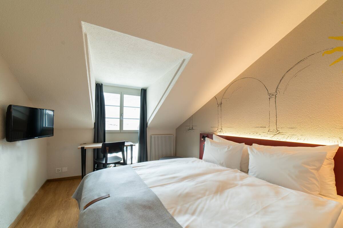 Una habitación de hotel con una cama, un escritorio, una silla, un televisor y una ventana.