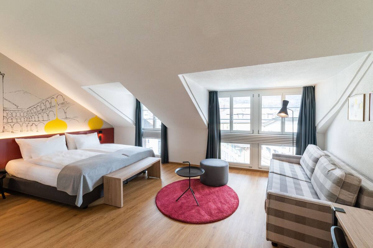 Una habitación moderna y bien iluminada con cama, sofá y una pequeña mesa.