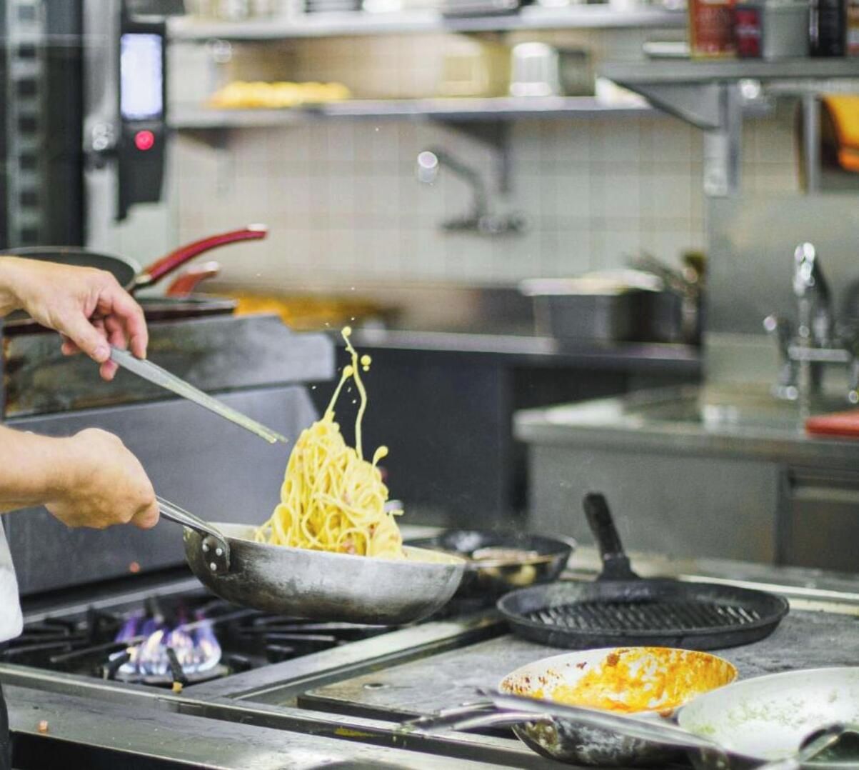 Una persona cocinando espagueti en una sartén sobre la hornilla.