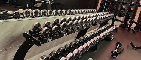 Un gimnasio con filas de mancuernas, discos de pesas y equipamiento de ejercicio.