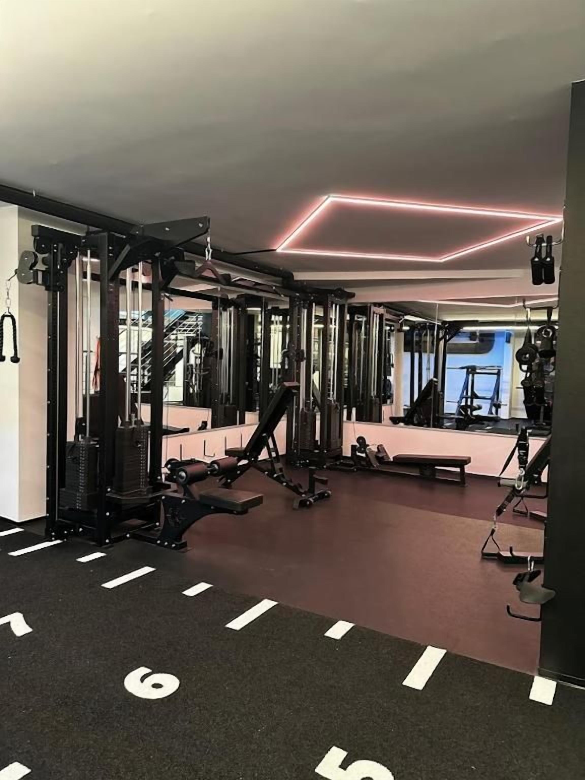 Une salle de sport équipée de matériel de musculation, de miroirs et dotée d’un sol recouvert d’une moquette rouge.