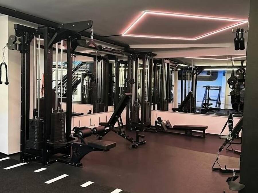 Une salle de sport équipée de matériel de musculation, de miroirs et dotée d’un sol recouvert d’une moquette rouge.
