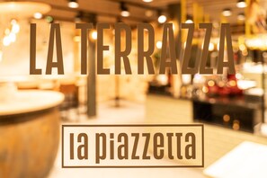 A blurred interior of a restaurant with the text "LA TERRAZZA" and "la piazzetta" indicating a terrace area. - Boutique Hotel Stockalperhof (Brig)