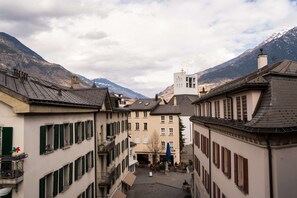 A narrow street with buildings on either side, a church with a bell tower, and mountains in the background. - Boutique Hotel Stockalperhof (Brig)
