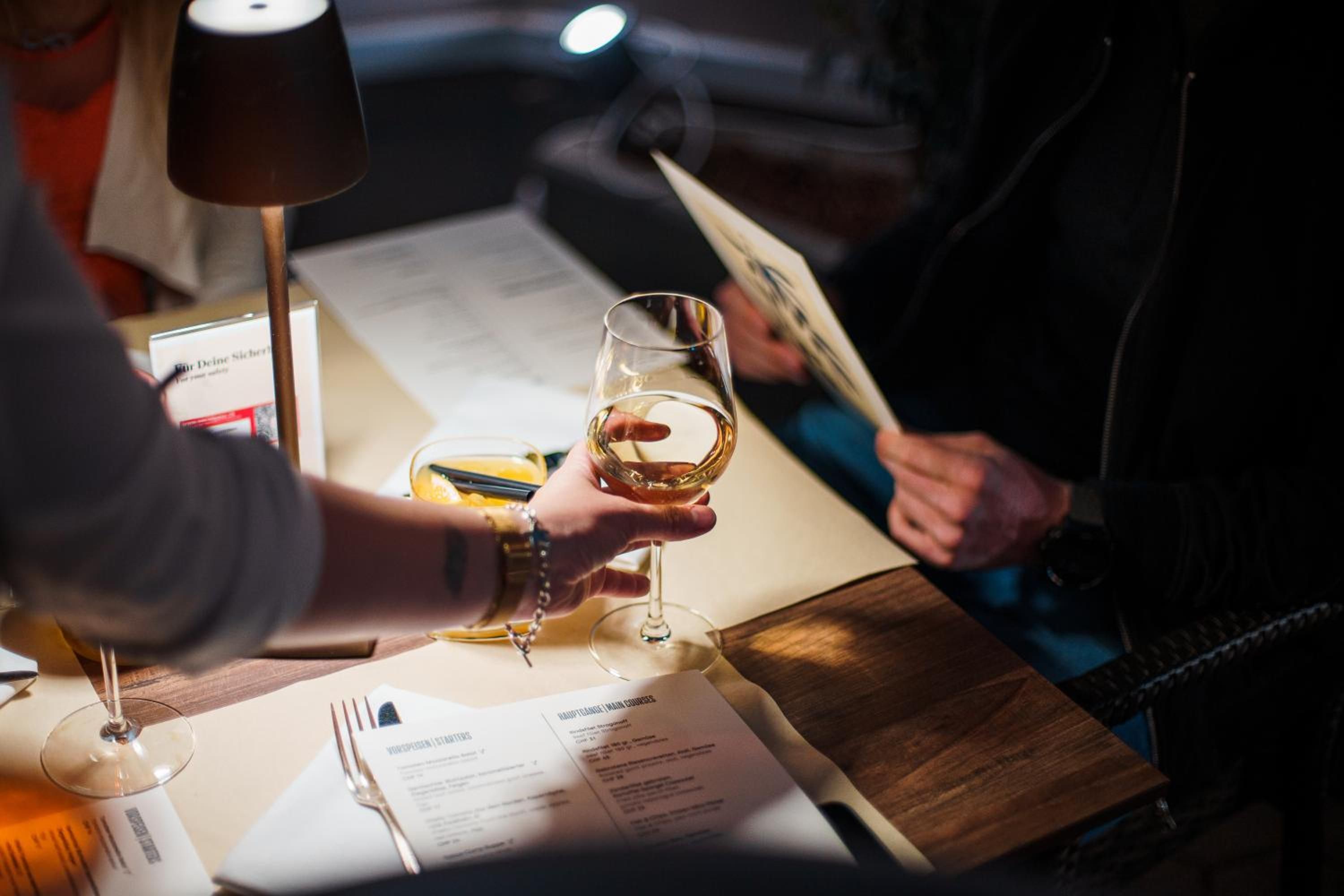 A person holding a wine glass, a menu, and a lamp on a table.