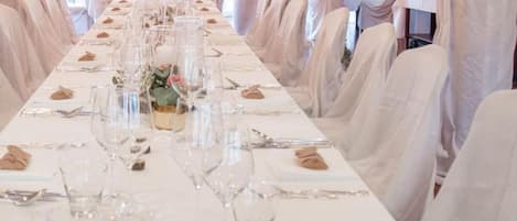 Una larga mesa de comedor dispuesta con manteles blancos, copas y servilletas.
