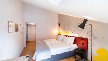 Ein modernes Hotelzimmer mit einem großen Bett, einem Schreibtisch und einem Sessel. Eine Tür führt in einen weiteren Raum.