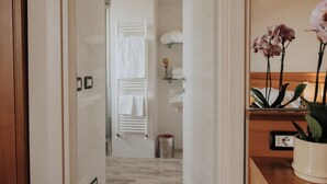 Un baño de hotel con ducha, toallero, lavamanos y un pequeño estante con artículos de aseo.