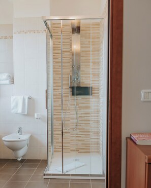 Un baño moderno con ducha envuelta en vidrio, lavamanos pedestal blanco y piso de baldosas.