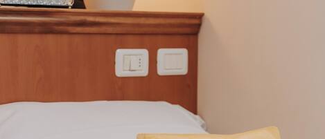 A bed with white bedding, a green and a beige pillow, a tissue box, and a potted plant on a wooden headboard.