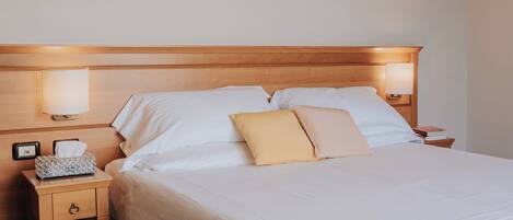 A neatly made bed with white linens, two bedside lamps, a nightstand with a tissue box, and a wooden headboard.