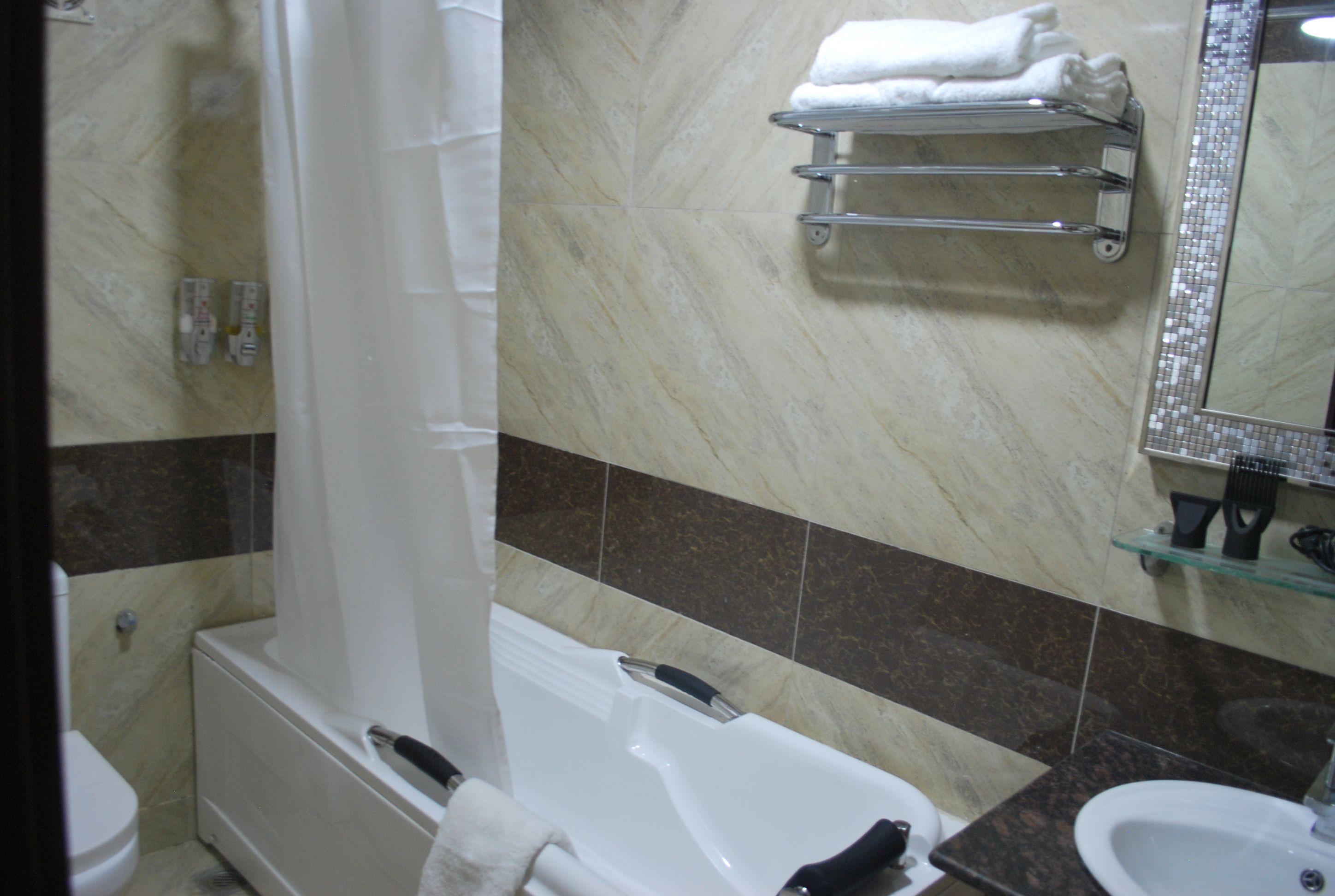 Une salle de bain avec une baignoire, des toilettes, un lavabo et une étagère en verre où sont posées des serviettes.